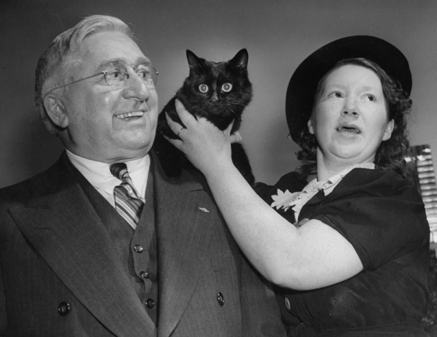 A black cat sits on a man's shoulder at an Anti-Superstition Party